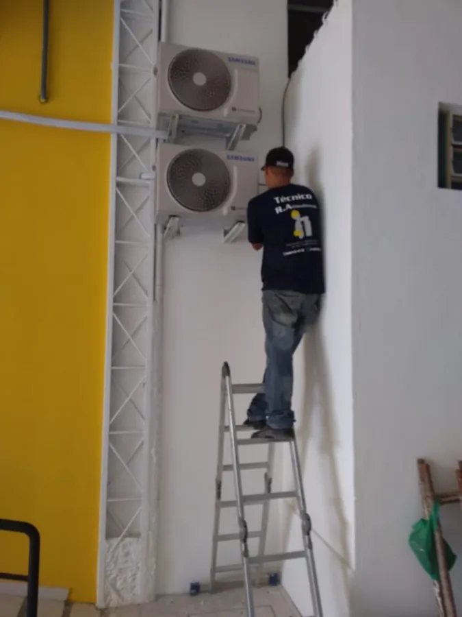 Técnico da R.A Climatização em uma escada instalando condensadoras em parede alta