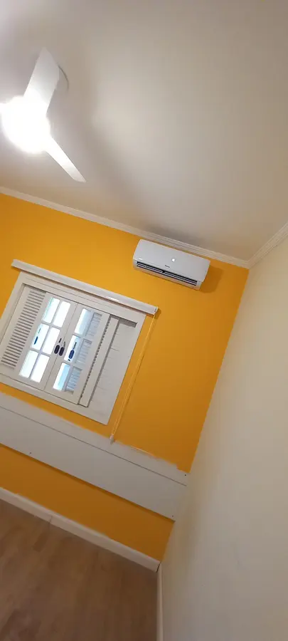 Split instalado acima da janela em quarto com parede amarela